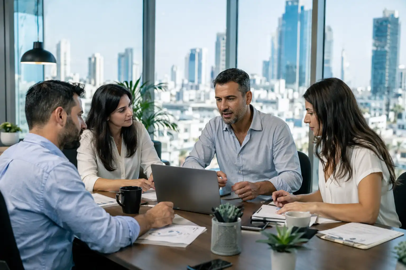 צוות במשרד באווירת שיתוף פעולה עם חלונות גדולים ונוף ברקע