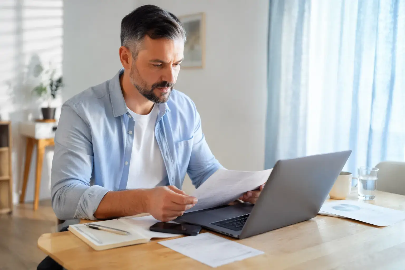 אדם בודק פוליסות ביטוח ומסמכים דרך מחשב נייד בסביבה ביתית מסודרת, להמחשת שירות הוזלת ביטוחים של אלוני פיין